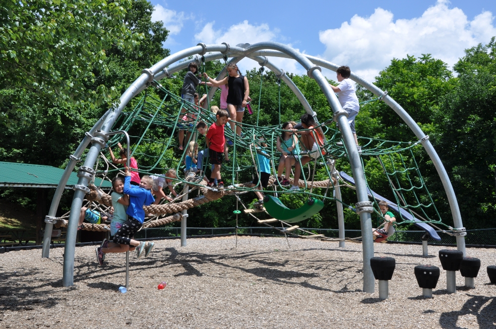 Children climb a large jungle gym at Mid County Park on a sunny summer day.