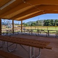 A view from under the picnic shelter shows the playground and ball fields with mountains and blue sky in the distance.