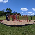 The playground at Motor Mile Park features slides, climbing areas, and a swing set with a mulch base in an open green space.