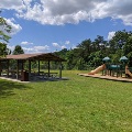 The playground and picnic shelter at Plum Creek Park are located next to each other and lined by trees and green space.