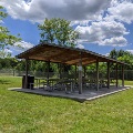 The picnic shelter at Plum Creek Park is in open green space with trees and the nearby baseball field.